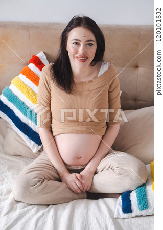 Pregnant woman gently touching her belly on a cozy bed. Pregnant woman gently touching her belly on a cozy bed. 120101832