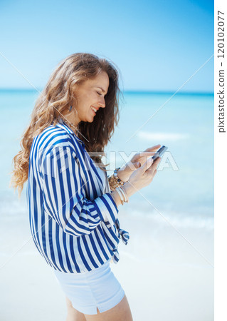 happy stylish woman on ocean coast with smartphone 120102077