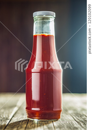 Glass bottle of ketchup on wooden table. Glass bottle of ketchup on wooden table. 120102099