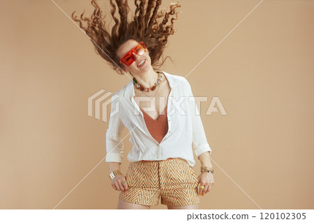 smiling trendy woman in blouse and shorts jumping on beige 120102305