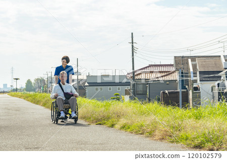 Senior man and female caregiver in wheelchair walking through the city 120102579