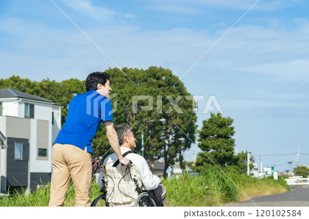 一位坐在輪椅上的老人和他的護理人員在鎮上散步的後視圖 一位坐在輪椅上的老人和他的護理人員在鎮上散步的後視圖 120102584