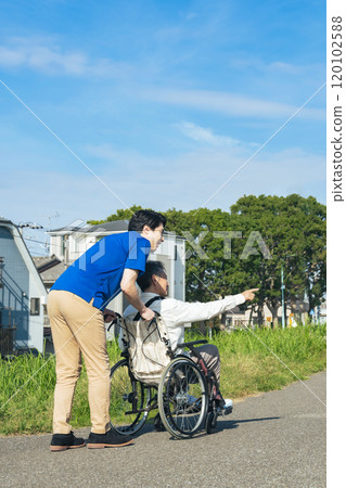 Rear view of a senior man in a wheelchair and his caregiver walking through the city 120102588