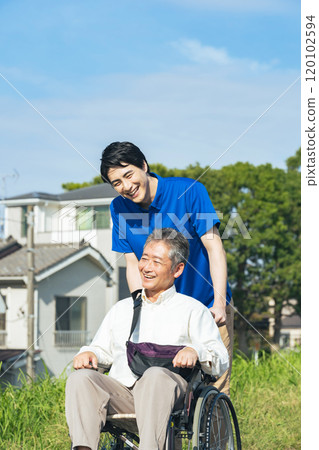 Senior man in a wheelchair and his caregiver walking through the city 120102594