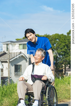 Senior man in a wheelchair and his caregiver walking through the city 120102595