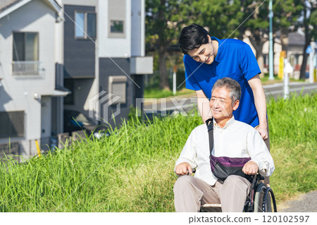 Senior man in a wheelchair and his caregiver walking through the city 120102597