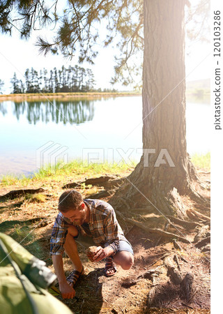 Setting up camp. Shot of a young man setting up a tent while on a camping trip. Setting up camp. Shot of a young man setting up a tent while on a camping trip. 120103286