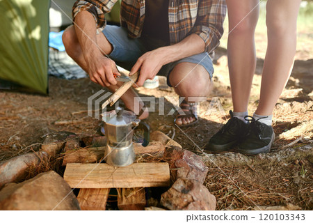 Putting on the morning coffee. Shot of campers preparing a campfire to make coffee. 120103343