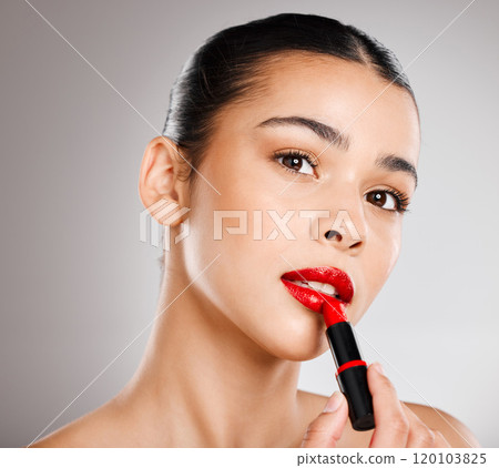 Red just looks so right. Studio shot of an attractive young woman applying red lipstick against a grey background. Red just looks so right. Studio shot of an attractive young woman applying red lipstick against a grey background. 120103825