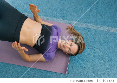 Young woman practicing fitness exercises on a yoga mat in a spacious gym environment 120104323