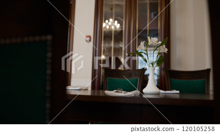 Cozy and minimalist restaurant design, close-up. Restaurant interior, flower in a small white vase on the table. A white vase with small flowers on the table next to the window and closet. 120105258