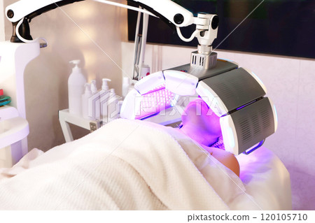 Photodynamic therapy. Young woman undergoes facial treatment using red LED in beauty salon. Concept of beauty and wellness. Photodynamic therapy. Young woman undergoes facial treatment using red LED in beauty salon. Concept of beauty and wellness. 120105710