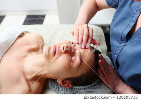 Beautiful young woman is undergoing facelift at beauty salon. Masseur does facial massage. Concept of beauty. Beautiful young woman is undergoing facelift at beauty salon. Masseur does facial massage. Concept of beauty. 120105716