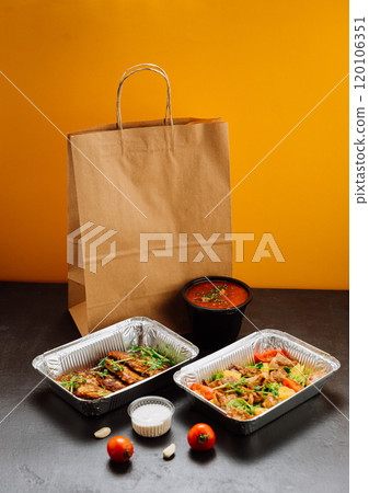 Food delivery packaging with trays of delicious meals, sauce containers, and paper bag  120106351