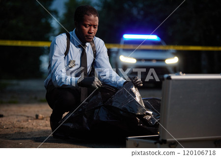 Full length of police officer closing body bag while investigating accident at night scene, copy space 120106718