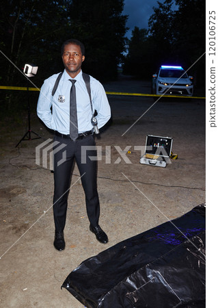 Vertical full length portrait of African American man as police officer standing at crime scene at nights and looking at camera Vertical full length portrait of African American man as police officer standing at crime scene at nights and looking at camera 120106725
