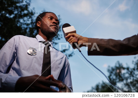 Low angle portrait of African American man speaking to microphone outdoors while giving comments for reporters, copy space 120106728