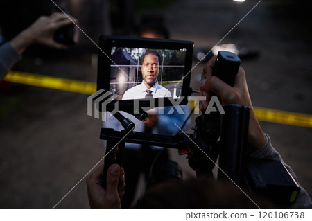 Portrait of policeman at video camera screen speaking to microphone while giving comments at crime scene, copy space 120106738