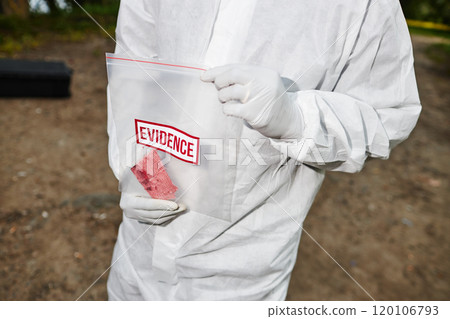 Closeup of man wearing protective suit holding plastic bag marked Evidence while working on crime scene, copy space 120106793