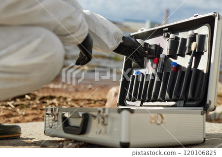 Close up of unrecognizable scientist wearing hazmat suit and using toolkit case while taking probes outdoors, copy space Close up of unrecognizable scientist wearing hazmat suit and using toolkit case while taking probes outdoors, copy space 120106825