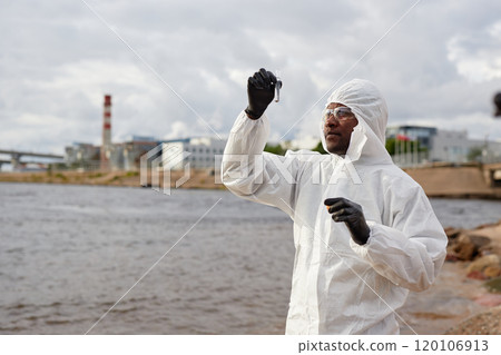 Waist up portrait of Black man as scientist wearing protective suit and holding test tube while doing probes on water quality outdoors, copy space Waist up portrait of Black man as scientist wearing protective suit and holding test tube while doing probes on water quality outdoors, copy space 120106913