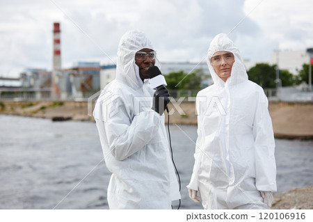 Waist up portrait of two news reporters wearing hazmat suits speaking to microphone working on industrial site and discussing ecology, copy space Waist up portrait of two news reporters wearing hazmat suits speaking to microphone working on industrial site and discussing ecology, copy space 120106916