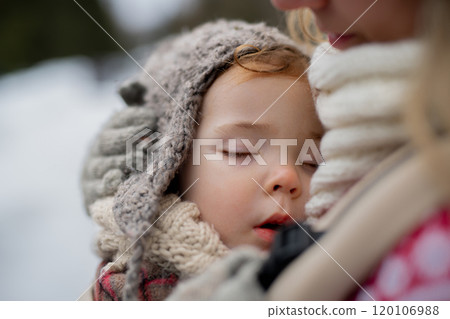 Mother standing in the middle of snowy landscape with sleeping daughter in baby carrier. Mom and girl enjoying winter holiday in the mountains. Mother standing in the middle of snowy landscape with sleeping daughter in baby carrier. Mom and girl enjoying winter holiday in the mountains. 120106988