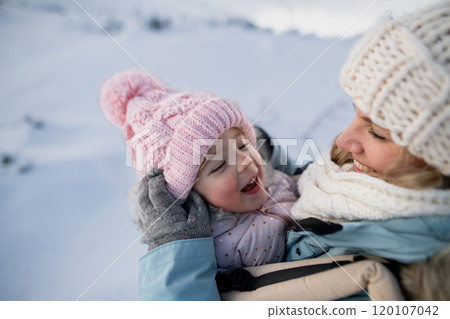 Mother standing in the middle of snowy landscape with daughter in baby carrier. Mom and girl enjoying winter holiday in the mountains. 120107042
