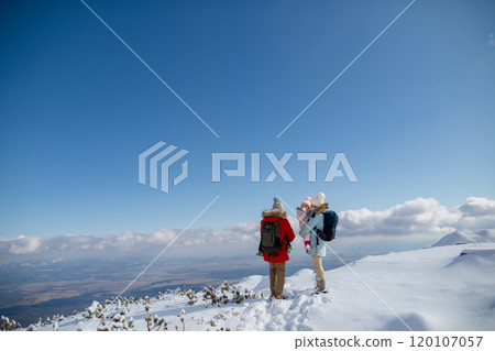 Parents with small kids standing in the middle of snowy landscape, looking at winter mountains and land under hill. Parents with small kids standing in the middle of snowy landscape, looking at winter mountains and land under hill. 120107057