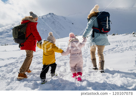 Young family is enjoying winter holiday in the mountains, holding hands while walking through the snowy landscape. Young family is enjoying winter holiday in the mountains, holding hands while walking through the snowy landscape. 120107078