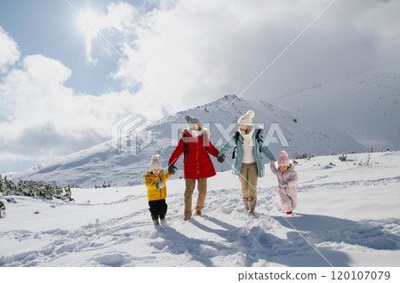 Young family is enjoying winter holiday in the mountains, holding hands while walking through the snowy landscape. 120107079