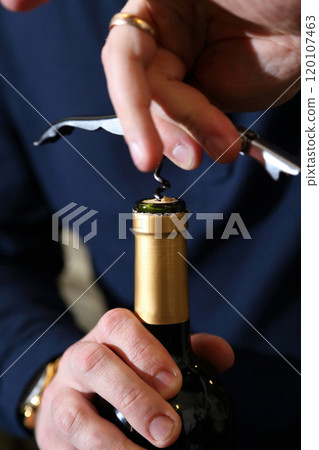 Red wine is uncorked with a sommelier's knife. Close-up of hands, cork, bottle neck. Wine is opened with a sommelier's knife. 120107463