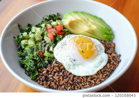 Nourishing grain bowl with wild rice, avocado, poached egg, and sauteed greens for healthy meal. 120108043