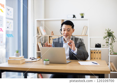 Asian businessman engaged in online video call wearing headset in office 120109700