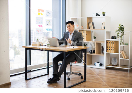 Asian businessman engaged in online meeting in modern office setting 120109716