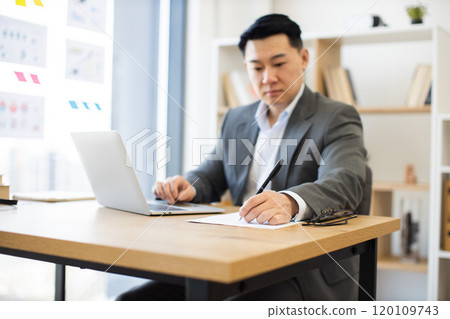 Asian businessman focused on writing report at office desk Asian businessman focused on writing report at office desk 120109743
