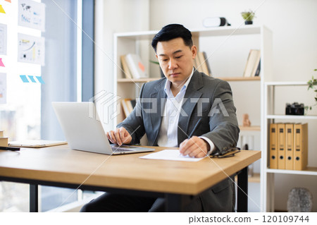 Asian businessman focused on laptop work in modern office setting Asian businessman focused on laptop work in modern office setting 120109744