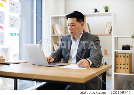 Focused Asian businessman working on laptop in modern office Focused Asian businessman working on laptop in modern office 120109745