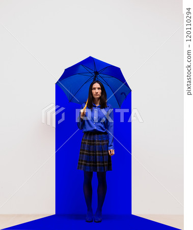 Woman dressed in blue standing under blue umbrella in blue square spotlight. Introspection, isolation, and resilience in minimalist setting. Contemporary art collage. Woman dressed in blue standing under blue umbrella in blue square spotlight. Introspection, isolation, and resilience in minimalist setting. Contemporary art collage. 120110294