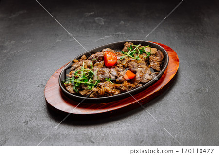 Sizzling beef liver with onions and fresh greens served on hot plate, perfect for a hearty meal 120110477