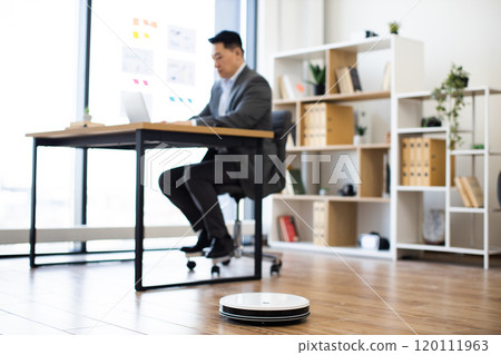 Asian businessman working in modern office with robot vacuum cleaner 120111963