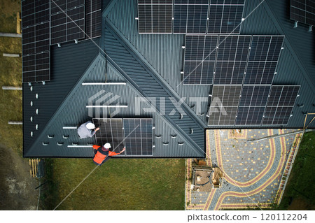 Electricians building photovoltaic solar module station on roof of house. Men technicians in helmets installing solar panel system outdoors. Concept of alternative and renewable energy. Aerial view. 120112204