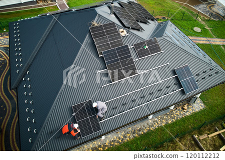 Builders building photovoltaic solar module station on roof of house. Men electricians in helmets installing solar panel system outdoors. Concept of alternative and renewable energy. Aerial view. Builders building photovoltaic solar module station on roof of house. Men electricians in helmets installing solar panel system outdoors. Concept of alternative and renewable energy. Aerial view. 120112212