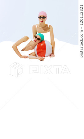 Two women wearing retro swim caps and sunglasses, posing with colorful beach ball on white background with blank space. 120112821