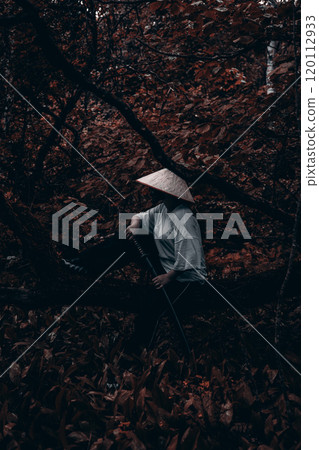 Samurai sits on a tree trunk in the forest and holds a katana on his lap. A lone samurai warrior dressed in traditional clothing rests in a quiet autumn forest, his hand resting on his katana. Samurai sits on a tree trunk in the forest and holds a katana on his lap. A lone samurai warrior dressed in traditional clothing rests in a quiet autumn forest, his hand resting on his katana. 120112933
