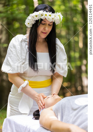Therapist female doctor making woman relaxing spa face massage with hands outdoors in the forest 120114491