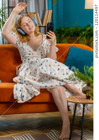 Happy young woman in wireless headphones relaxing lying on sofa at home listening favorite music Happy young woman in wireless headphones relaxing lying on sofa at home listening favorite music 120114497