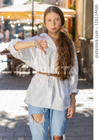 Upset child girl woman showing thumbs down sign, disapproval, dissatisfied bad work, mistake in city Upset child girl woman showing thumbs down sign, disapproval, dissatisfied bad work, mistake in city 120114498