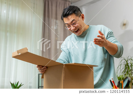 Happy Chinese man shopper unpacking cardboard box delivery parcel online shopping purchase at home Happy Chinese man shopper unpacking cardboard box delivery parcel online shopping purchase at home 120114555