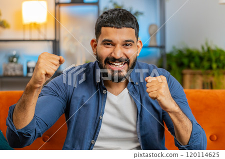Happy Indian young man watching TV celebrating success winning good news lottery game luck victory Happy Indian young man watching TV celebrating success winning good news lottery game luck victory 120114625